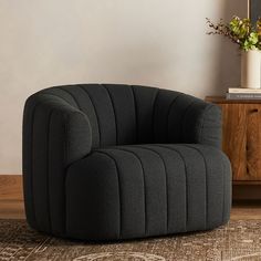 a black chair sitting on top of a wooden floor next to a vase filled with flowers