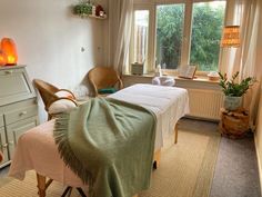 a massage room with two beds and a table in front of a large window that has plants on it