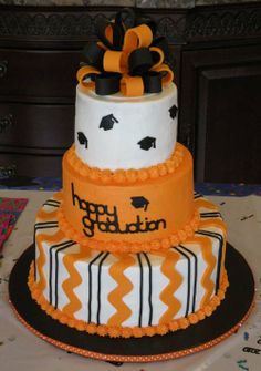 a three tiered cake decorated with orange and black ribbon, on top of a table