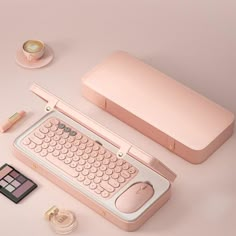 a pink computer keyboard sitting on top of a table next to other items and makeup