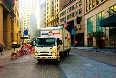 a delivery truck driving down a city street next to tall buildings with people walking on the sidewalk