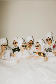 four women in white robes and sunglasses are sitting on a bed with their hair dryers wrapped around them