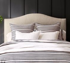 a bed with black and white striped comforter on top of it next to a potted plant