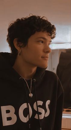 a young man with curly hair wearing a black boss hoodie and looking off to the side