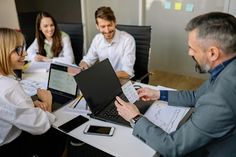 three people sitting at a table with laptops in front of them and papers on the desk