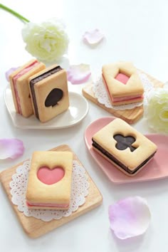 small cakes with hearts on them are sitting on plates next to pink flowers and petals