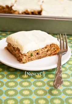 a piece of carrot cake with frosting on a plate next to a knife and fork