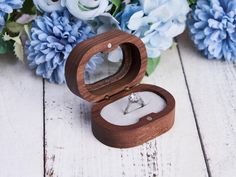 an open wooden ring box with a diamond in it and blue flowers around the edges