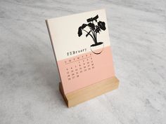 a calendar sitting on top of a wooden stand next to a plant in a vase