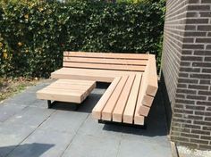 a wooden bench sitting on top of a stone walkway next to a brick wall and shrubbery