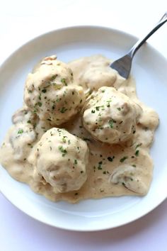 a white plate topped with meatballs covered in gravy next to a fork