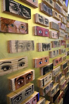 a woman standing in front of a wall covered with wooden boxes and eyeballs on them