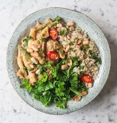 a white bowl filled with rice, chicken and veggies on top of a table