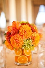 a vase filled with oranges and flowers on top of a table next to glasses