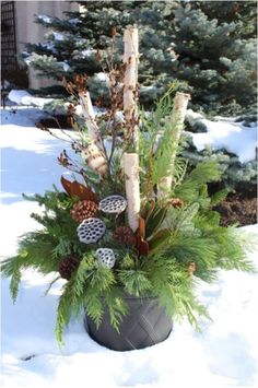 a planter filled with pine cones and other plants in the middle of snow covered ground