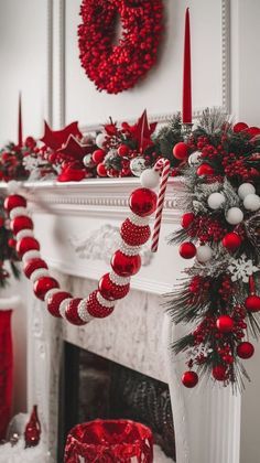 red and white christmas decorations in front of a fireplace with wreaths on the mantle