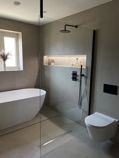 a white bath tub sitting next to a toilet in a bathroom under a large window