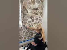 a woman is painting a stone wall in her home