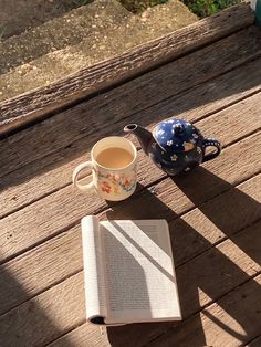 an open book sitting on top of a wooden table next to a cup of coffee