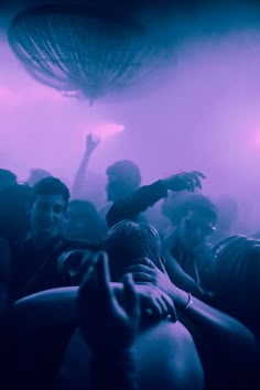 a group of people standing around each other in front of a purple light with their arms up