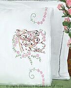 two white pillows sitting on top of a bed next to a vase with pink flowers