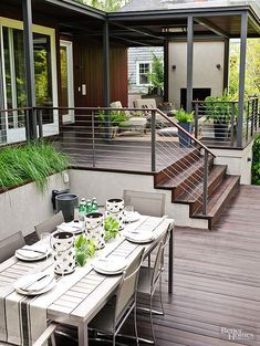 a table with plates and cups on it in front of a deck that has stairs leading up to the upper level