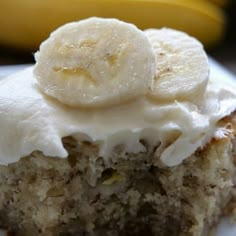 a piece of banana cake with frosting and sliced bananas on top, sitting on a plate