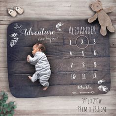 a baby laying on top of a wooden floor next to a teddy bear and calendar