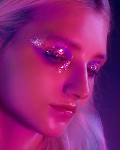 a woman with bright makeup and glitter on her face is looking at the camera while wearing pink