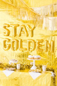 a table topped with cake and cupcakes next to a gold foil sign that says stay golden