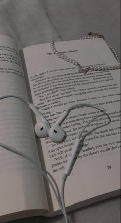 an open book with headphones laying on it's side next to a pair of earbuds