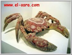 an intricately decorated crab on display in a white room with no one around it