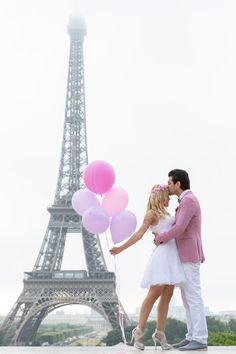 a man and woman standing in front of the eiffel tower with pink balloons