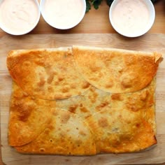 an overhead view of some food on a cutting board with bowls and dips in the background