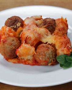 a white plate topped with meatballs covered in sauce and garnished with green leaves