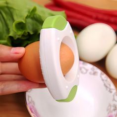 an egg seperator being held by a woman's hand next to eggs and lettuce