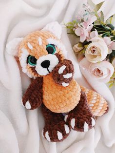 a crocheted stuffed animal laying on top of a white blanket next to flowers