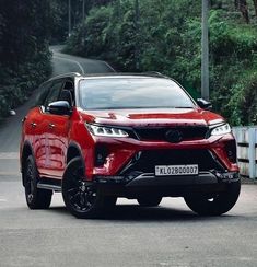 a red suv parked on the side of a road next to some bushes and trees