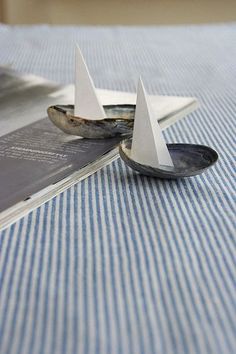 two small paper boats sitting on top of a blue and white table cloth with an open book in the background