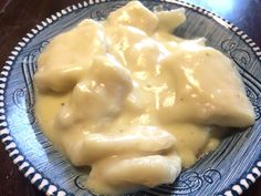 a blue and white plate topped with ravioli covered in cheese sauce on top of a wooden table