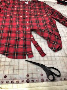 a pair of scissors are laying next to a red plaid shirt on a cutting board