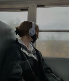 a woman with headphones sitting on a train looking out the window at the scenery