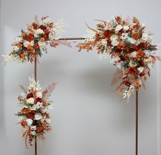 three tall floral arrangements on metal poles against a white wall