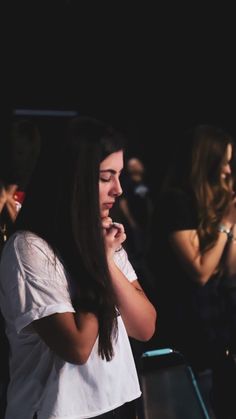 a woman standing in front of a crowd with her hands clasped to her chest and looking down