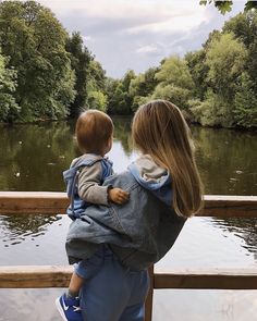 a woman carrying a child on her back while looking out over the water at trees