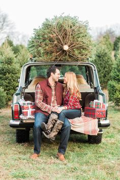 a man and woman sitting in the back of a truck with christmas trees on top