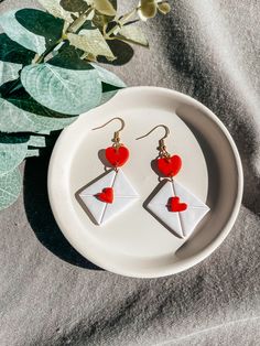 a pair of red and white earrings sitting on top of a plate next to a plant