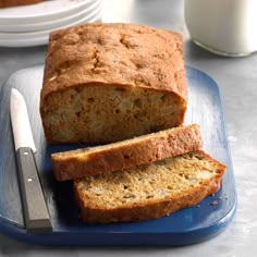 a loaf of banana bread on a blue plate with a knife and glass of milk