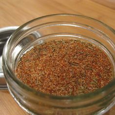 a glass jar filled with spices sitting on top of a wooden table next to a metal container