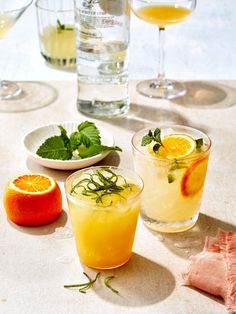 three glasses filled with drinks sitting next to grapefruits and oranges on a table